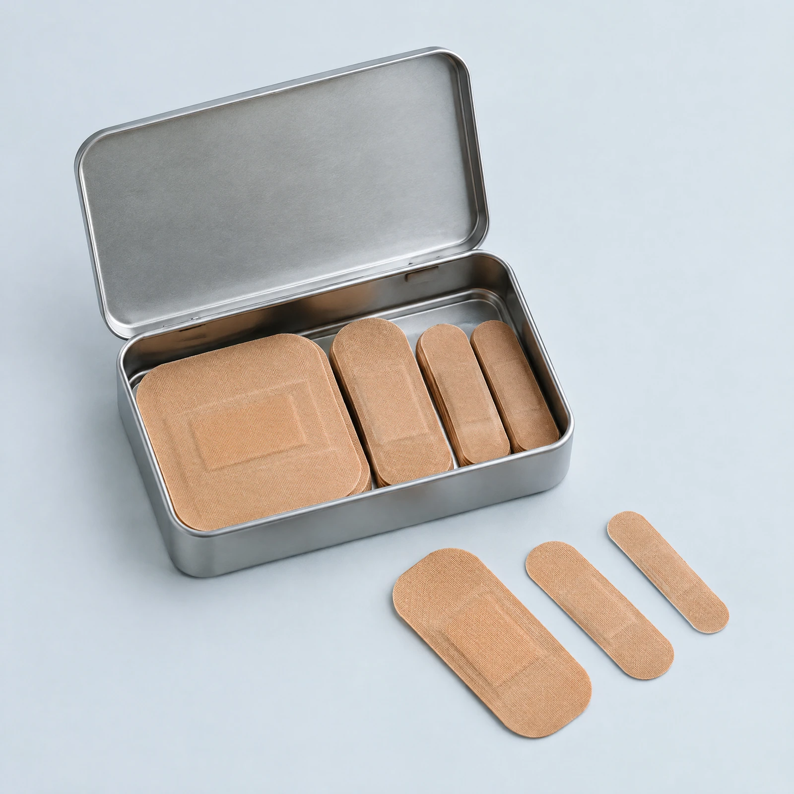 Open silver-tone tin of tan adhesive bandages in several sizes with three bandages laid beside it