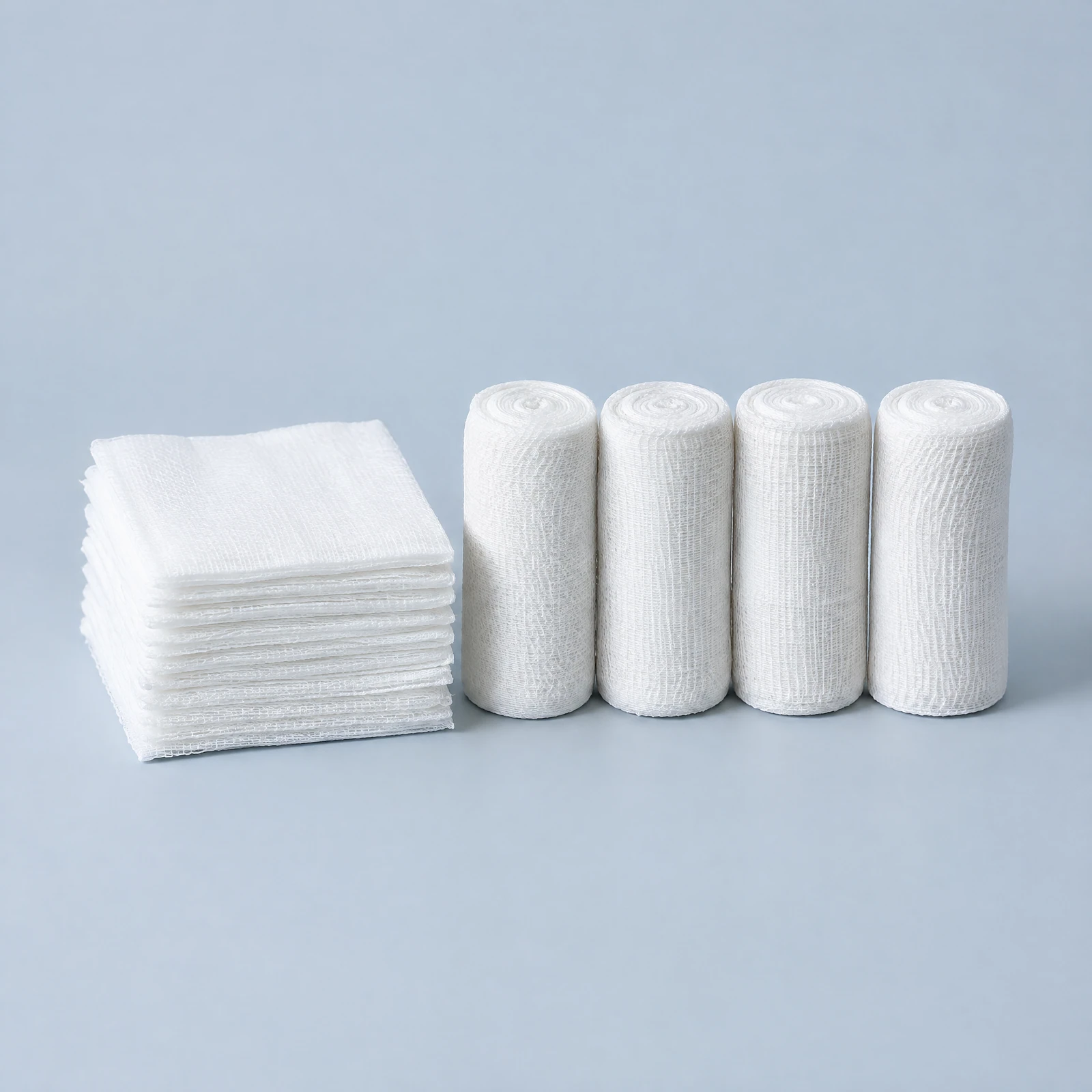 Stack of white square gauze pads beside four rolled white gauze bandages